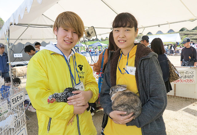 写真:動物愛護フェスティバルの様子。犬のきぐるみの横で笑顔でピースをしている学生。