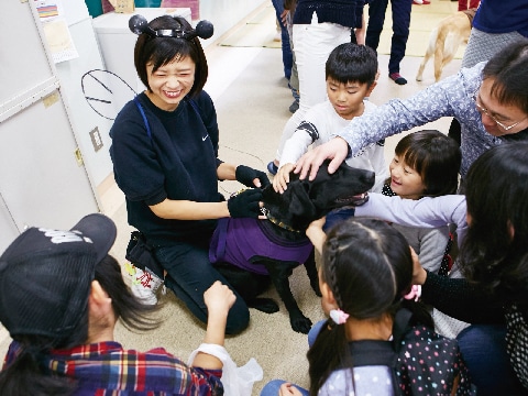 お客さんに囲まれ触れ合う学内犬と女子学生